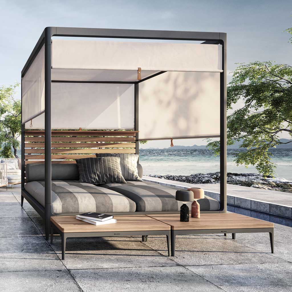 Image of Gloster Grid Cabana daybed with striped cushions, white adjustable blinds and teak topped tables in the foreground