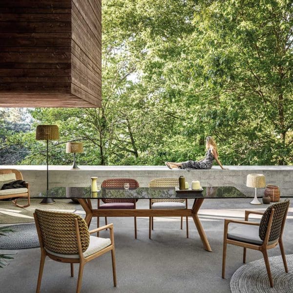 Image of Kay teak and wicker garden dining chairs around a Gloster outdoor table on a shady terrace