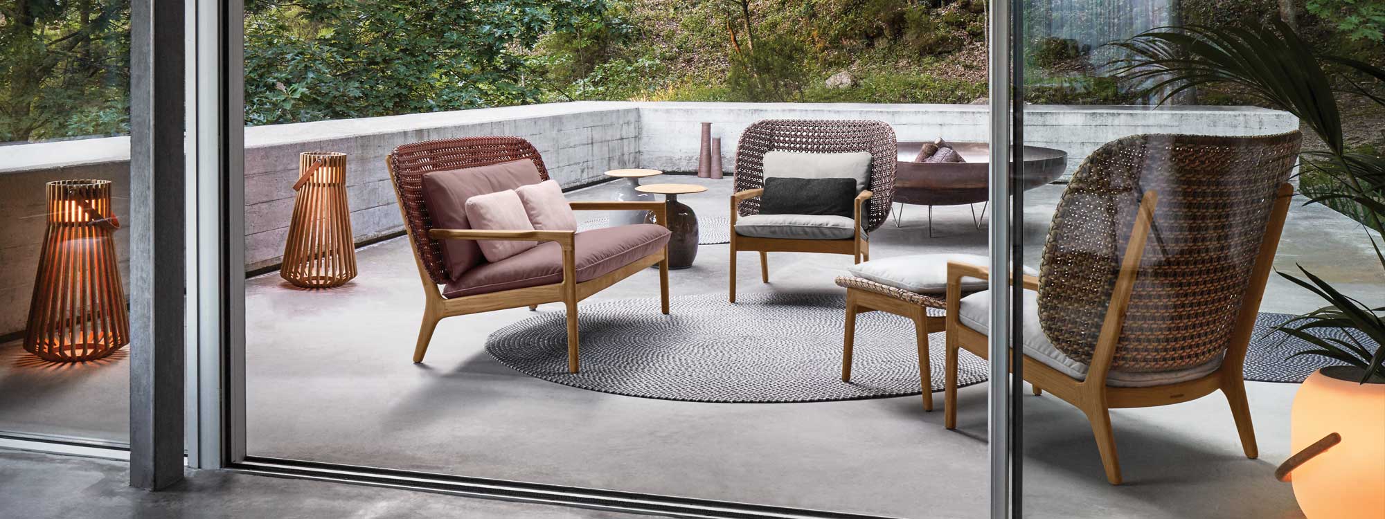Image of Gloster Kay wicker garden sofa and lounge chairs, together with Ray lantern on terrace at dusk