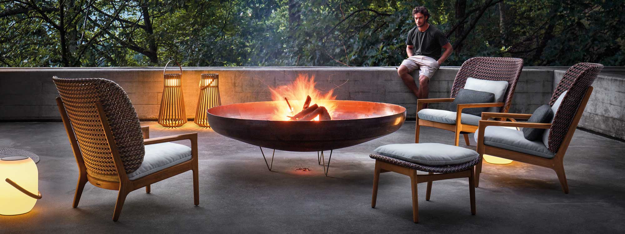 Image of Gloster Kay modern garden lounge furniture on terrace, placed around fire pit with dancing flames within