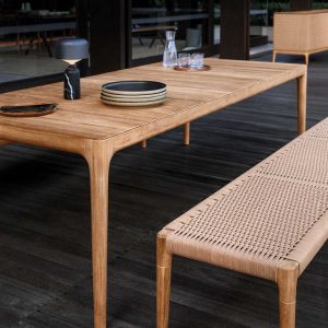 Image of Gloster Lima teak garden table with Lima teak bench with woven all-weather wicker surface