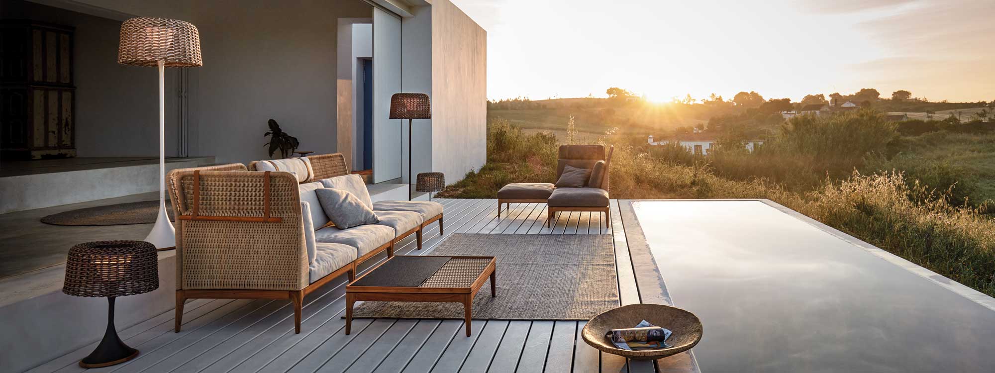 Image at dusk of Gloster Lima contemporary wicker garden sofa and Mesh garden lights