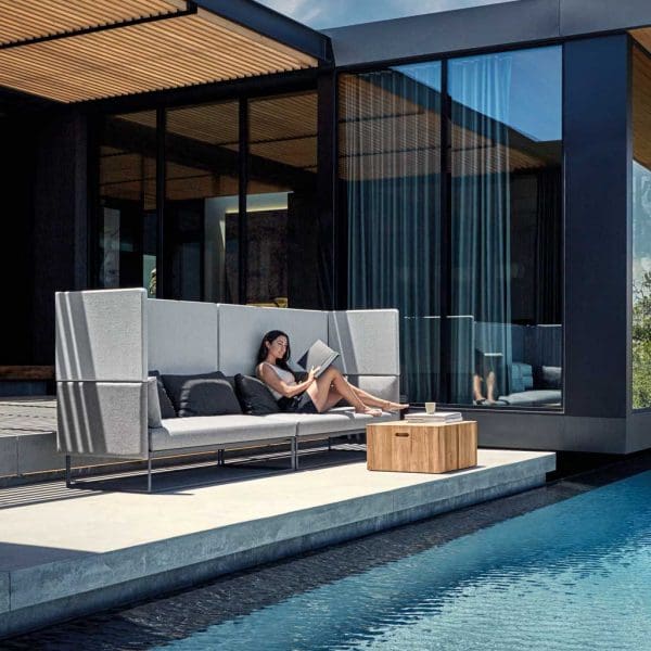 Image of woman sat reading in seclusion and comfort of Maya Cove garden sofa by Gloster next to inviting swimming pool