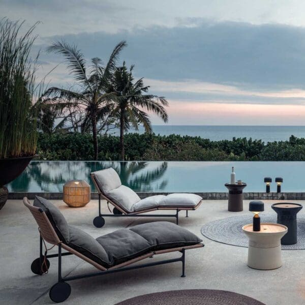 Image of pair of Zenith ergonomic sun loungers by Gloster with silhouette of palm trees in the dusk sky in the background