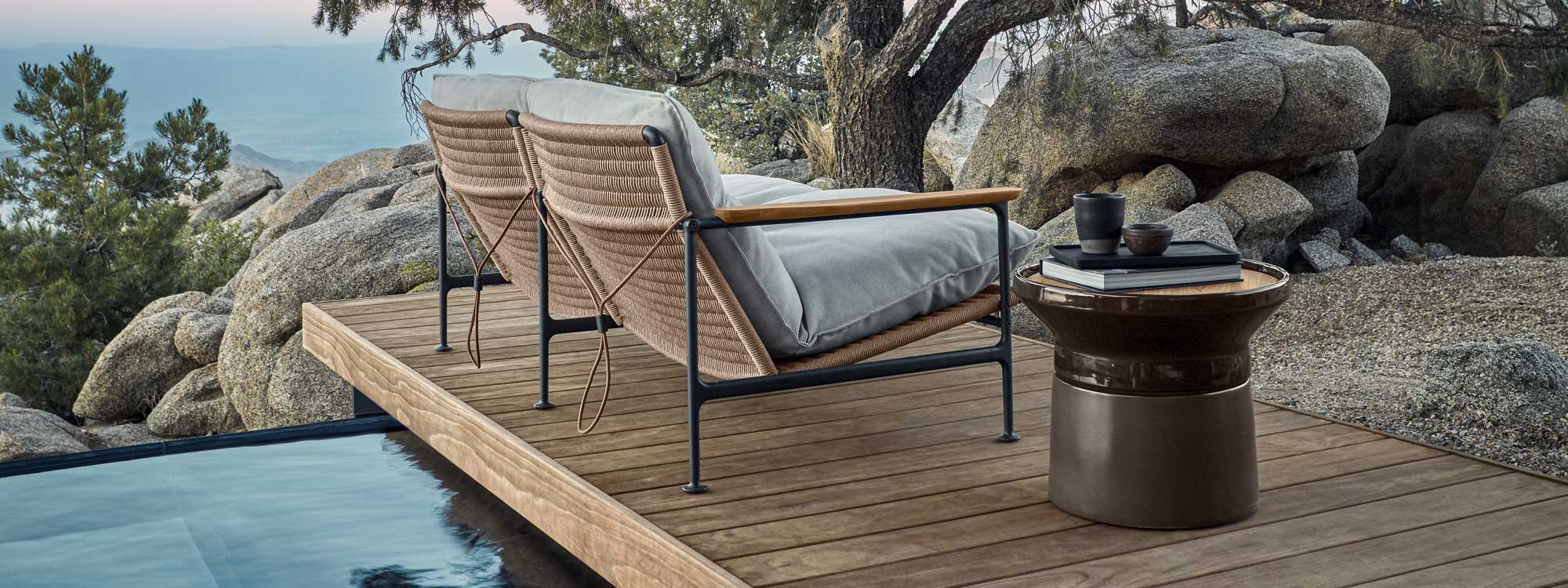 Image of rear of Gloster Zenith lounge chair in meteor-coloured aluminium and wheat-coloured synthetic wicker, together with Coso modern side table