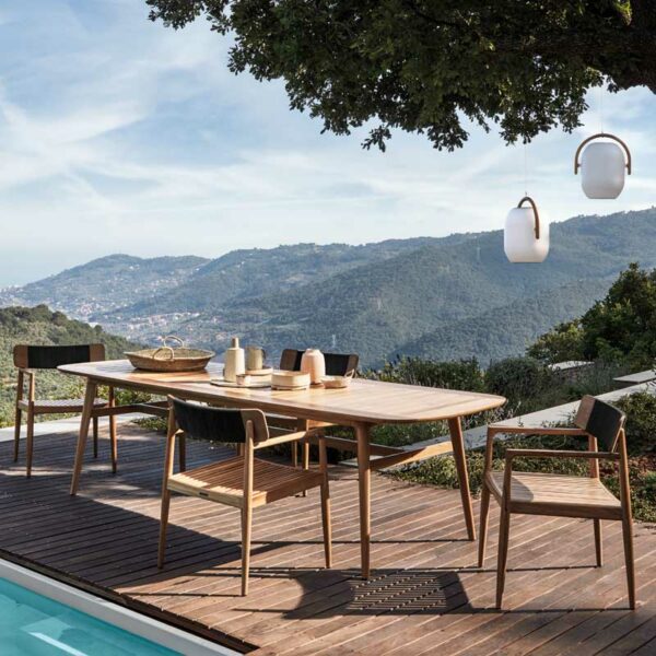 Image of Gloster contemporary teak chairs and Gloster rectangular teak table on sunny poolside with dramatic hills in the background