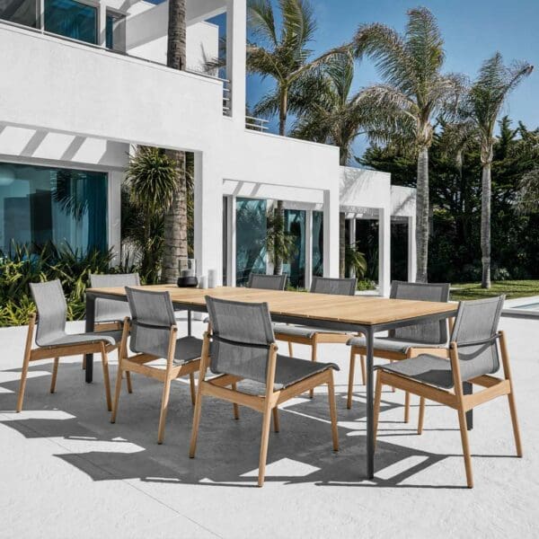 Image of Sway armless teak chairs and Gloster contemporary teak garden table on sunny terrace with palm trees and house in the background
