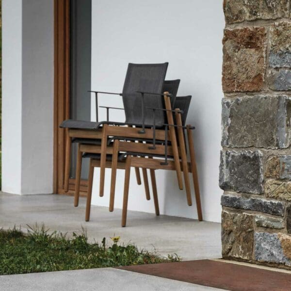 Image of stacked Sway luxury teak chairs by Gloster against white wall