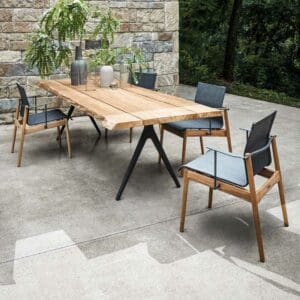 Image of Sway teak garden armchairs with grey seat & back next to Raw planked teak outdoor table by Gloster