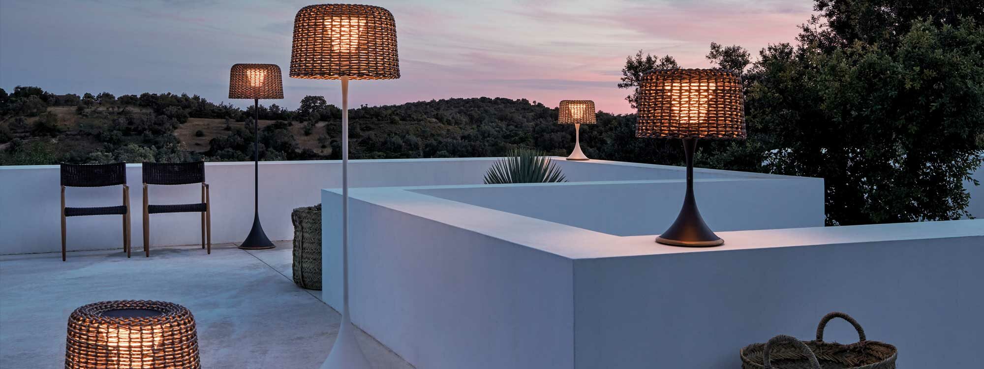 Image of different sizes of Gloster Ambient Mesh table lamps and garden floor lamps on white-washed rooftop at dusk