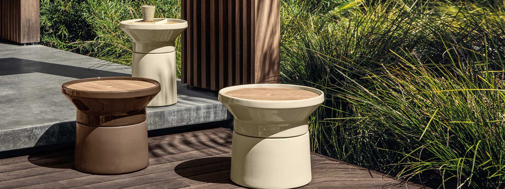 Image of different sizes of Coso outdoor low tables in sand and earth glazed ceramic finishes by Gloster, with architectural grasses in the background