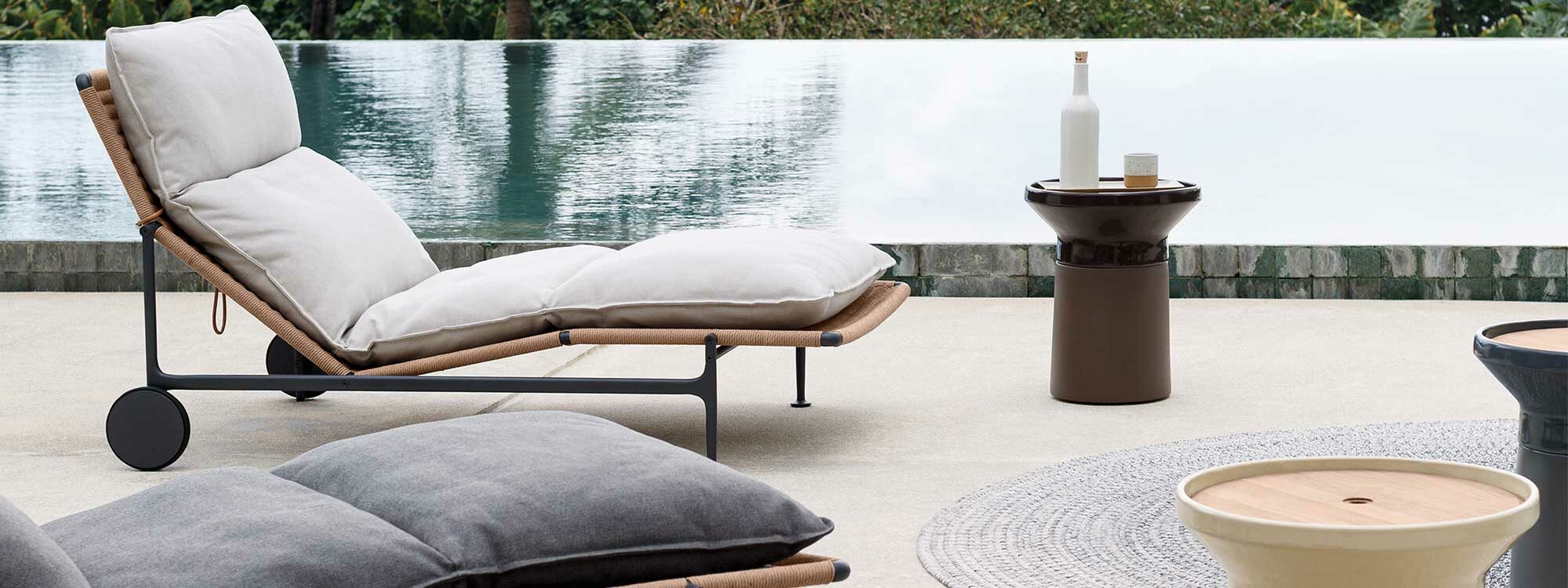 Image of Gloster Zenith sun loungers and Coso modern ceramic occasional tables next to tranquil waters of horizon swimming pool at dusk