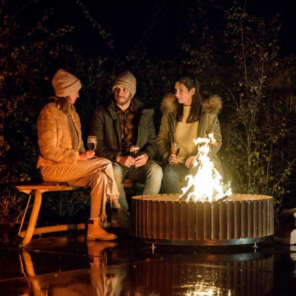 Nighttime image of friends sat drinking beer on The Circle round garden bench whilst sat around the flames of The Ring corten fire bowl