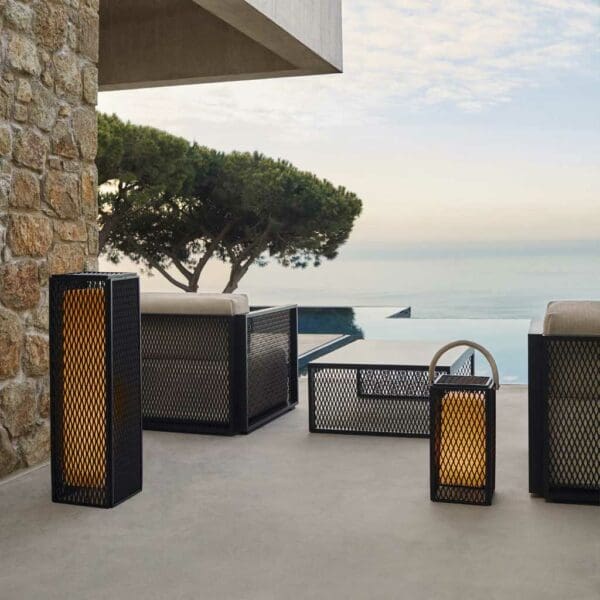 Image of Vondom The Factory modern garden lanterns and sofa on terrace at dusk, with swimming pool, sea and hazy sky in the background