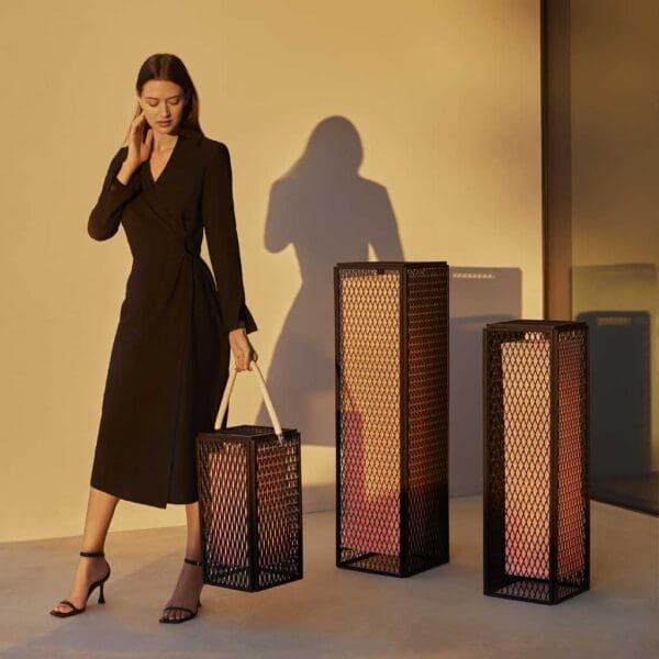 Image of woman carrying small The Factory LED garden lantern next to 2 larger outdoor lamps.