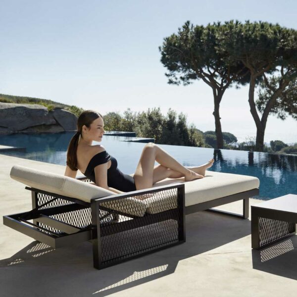 Image of woman relaxing on The Factory sunbed by Vondom, on sunny poolside with cedar tree, blue sea and sky in the background