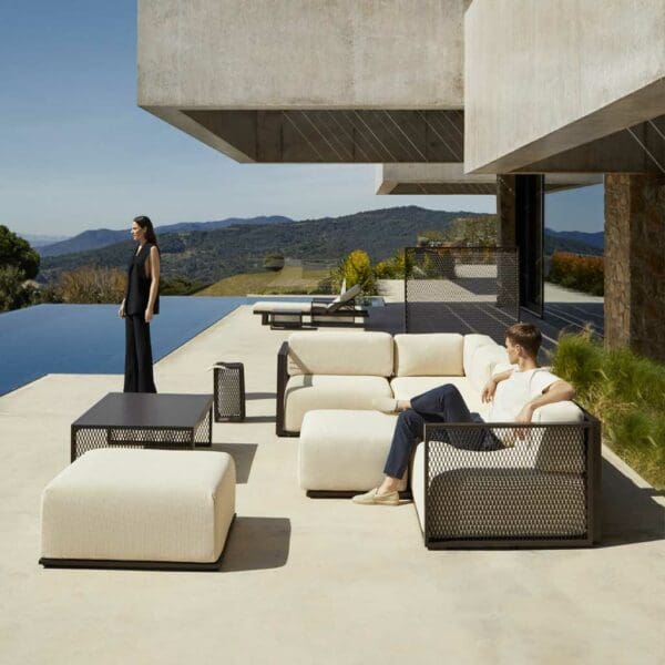 Image of couple relaxing around Vondom The Factory sectional garden sofa on terrace, with swimming pool and green hills in the background