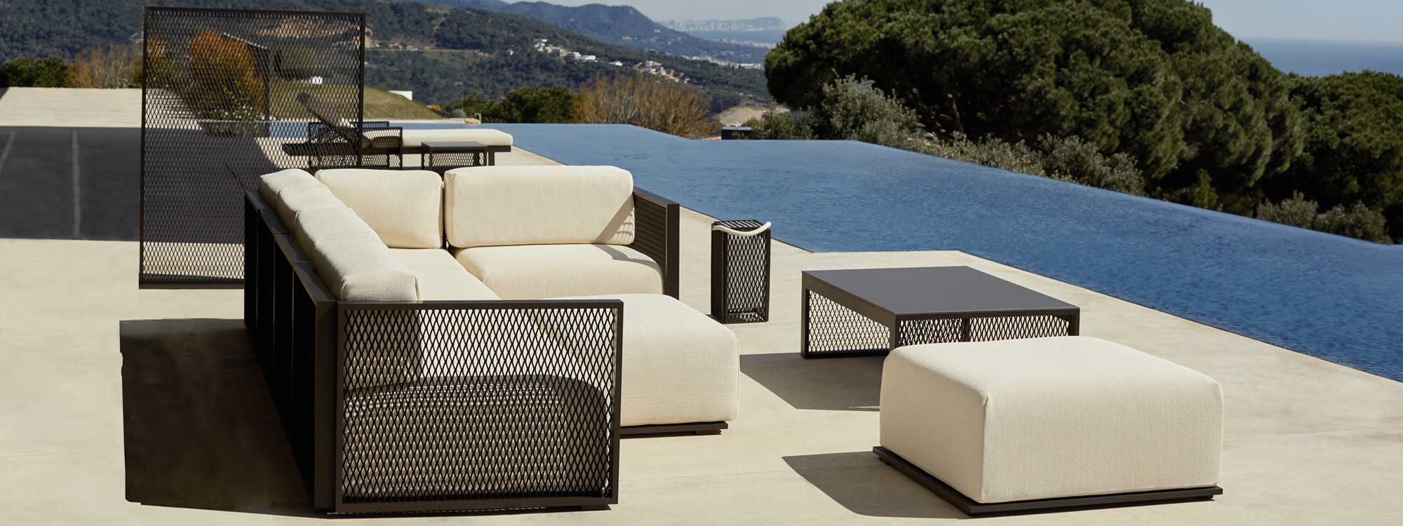 Image of Vondom The Factory modern garden corner sofa and lounge chair on sunny poolside with hills dropping to the coast in the background