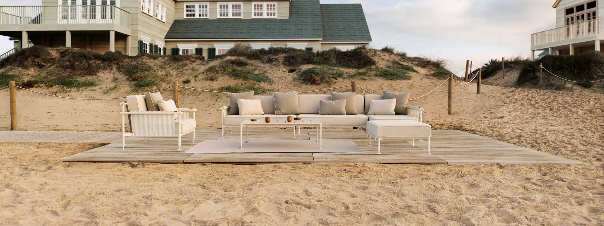 Image of Vondom Hamptons sectional garden sofa on wooden decking on the beach, with large beachside house in the background