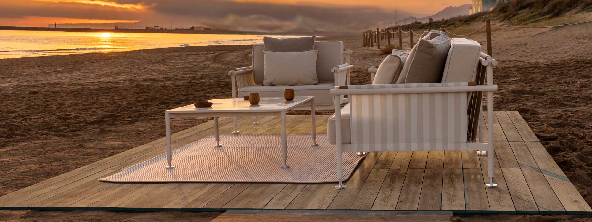 Image of pair of Hamptons exterior lounge chairs by Vondom, on wooden decking on beach at dusk