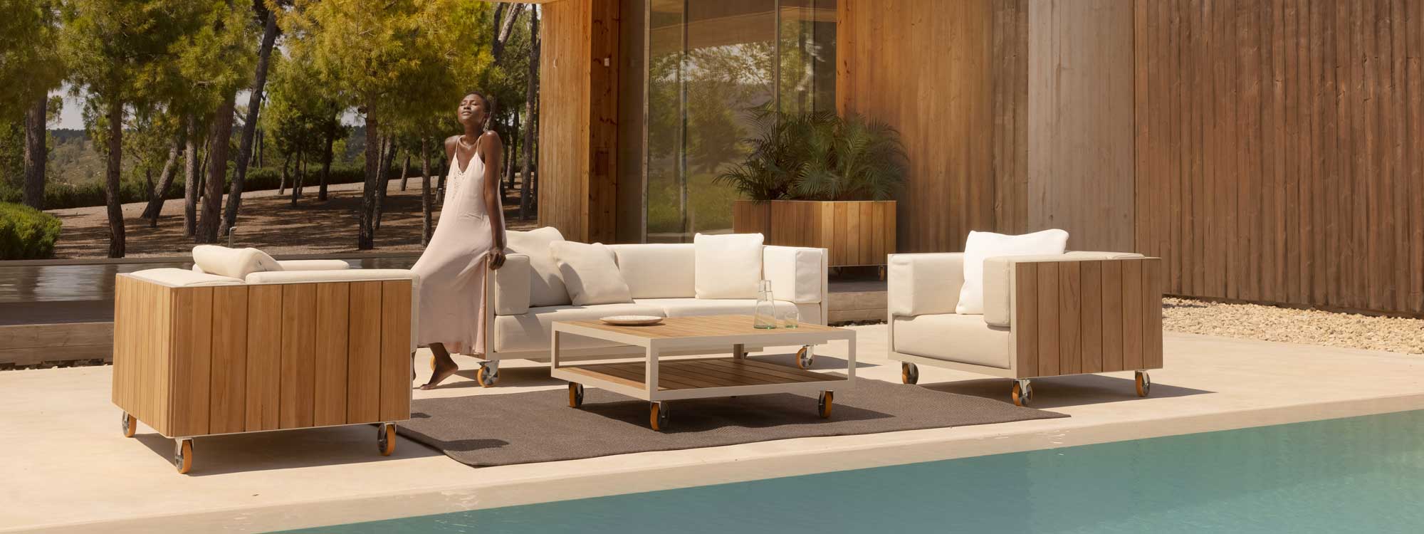 Image of woman sat on the arm of Vineyard garden sofa with wheels by Vondom on minimalist poolside