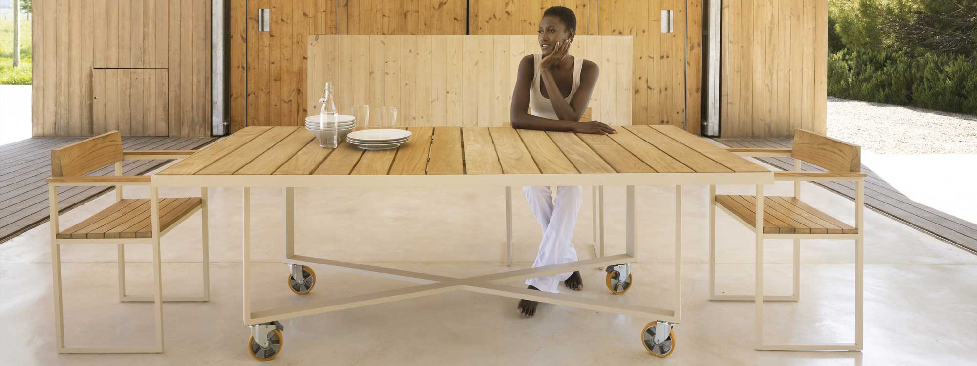 Image of woman sat at Vondom Vineyard modern garden table with wheels, inside a minimalist garden room