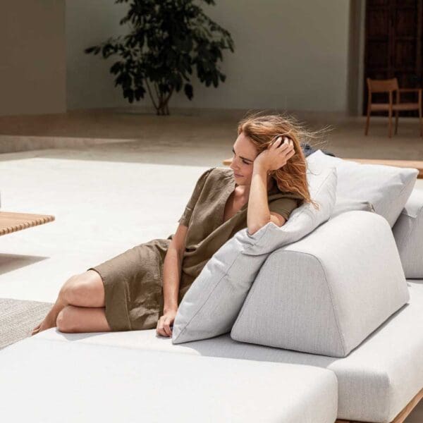 Image of woman lying back in the sun whilst resting on the self-supporting back cushion of Deck teak garden sofa by Gloster