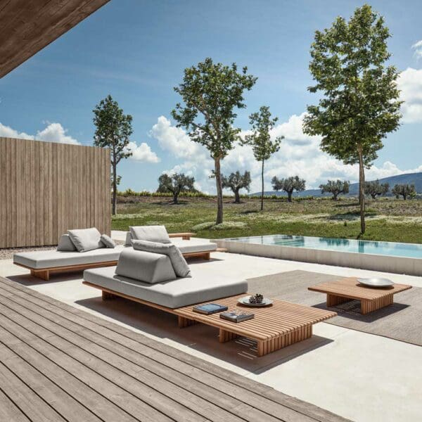 Image of Gloster Deck contemporary teak garden sofa on sunny poolside, with trees and countryside in the background