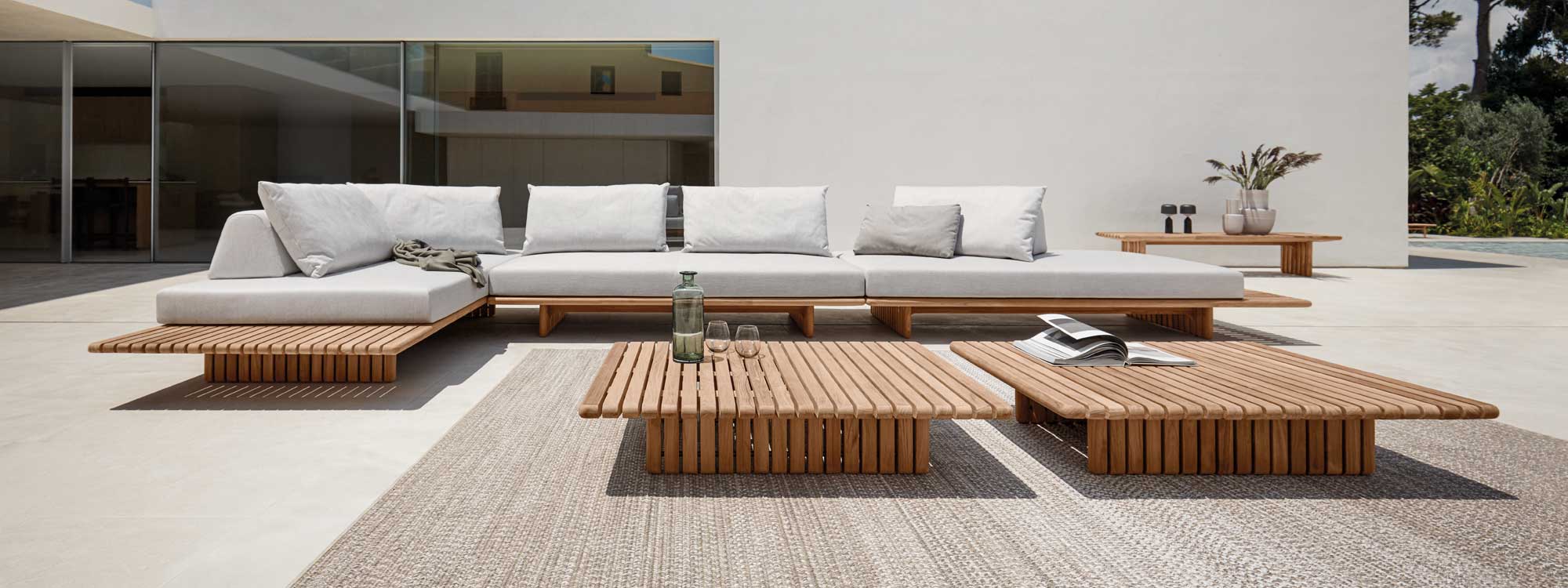 Image of Gloster Deck minimalist teak corner sofa on sunny terrace with central coffee table on an outdoor rug