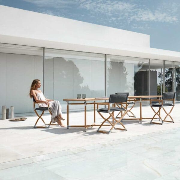 Image of woman on terrace sat in Navigator folding teak director next to folding teak tables