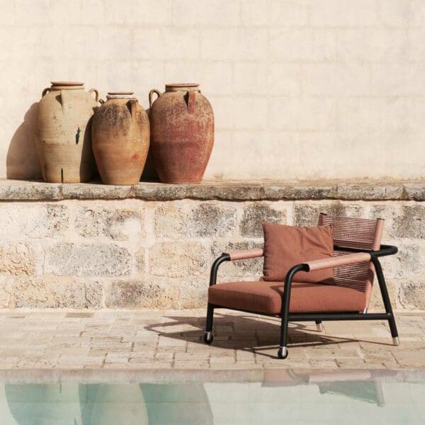 Image of RODA Astra garden recliner with smoke coloured frame and terracotta cushions, with large terracotta pots in the background and reflective waters of swimming pool in the foreground