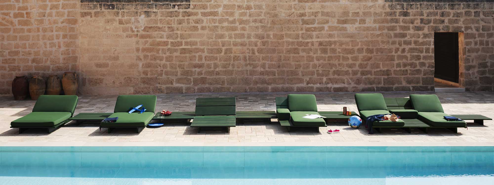 Image of row of 6 Eolie minimalist sun loungers and low tables in olive-coloured iroko hardwood by RODA, shown on poolside