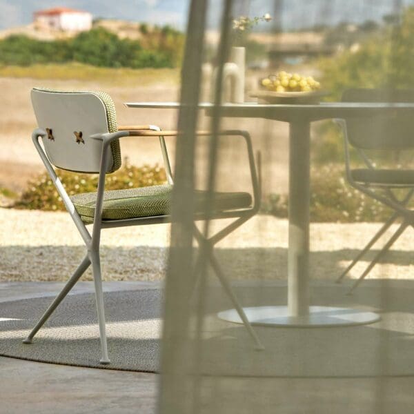Image of Exes garden chairs in white aluminium and teak, shown next to Butler circular dining table by Royal Botania, with drape gently billowing in the foreground