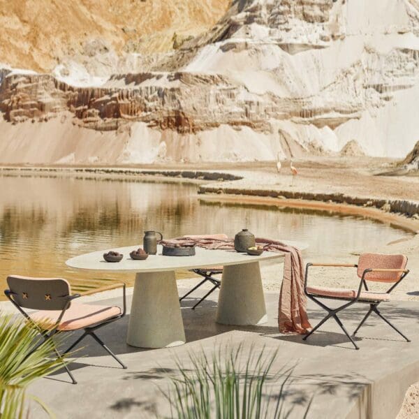 Image of Royal Botania Exes low armchairs and Conix elliptical low dining table on sunny terrace with water and rockface in the background