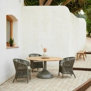 Image of Cane-line Derby garden dining chair and Glaze round teak table with whitewashed wall in the background