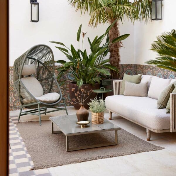 Image of Cane-line Moments sand-coloured garden sofa, Hive garden chair and Glaze low table in peaceful courtyard with exotic plants and palm in the background