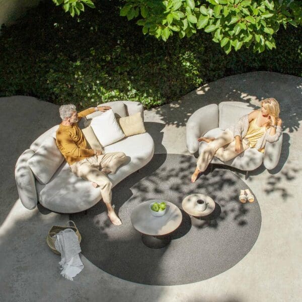Image of a couple relaxing and chatting on Organix garden sofa and lounge chair, beneath dappled shade of a tree