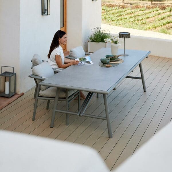 Image of woman sat reading at Cane-line Sticks table on decked terrace