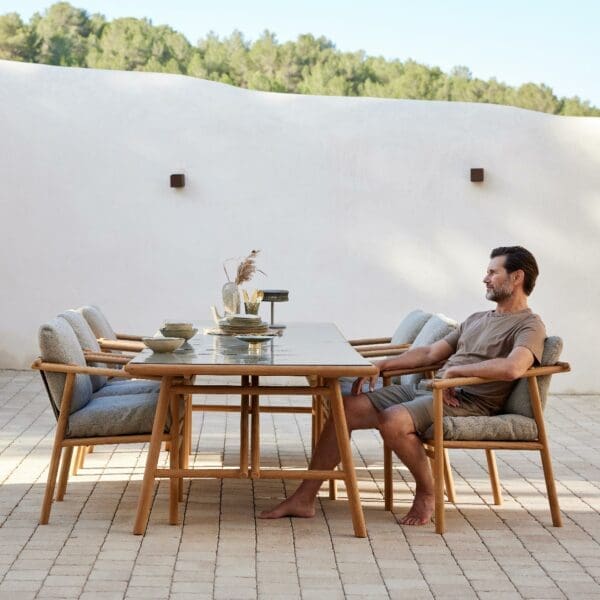 Image of man sat contemplating at Sticks FSC teak dining set on terrace, with whitewashed wall in the background
