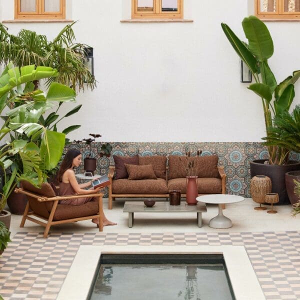 Image of Sticks teak garden sofa, with exotic plants either side and peaceful waters of rill in the foreground