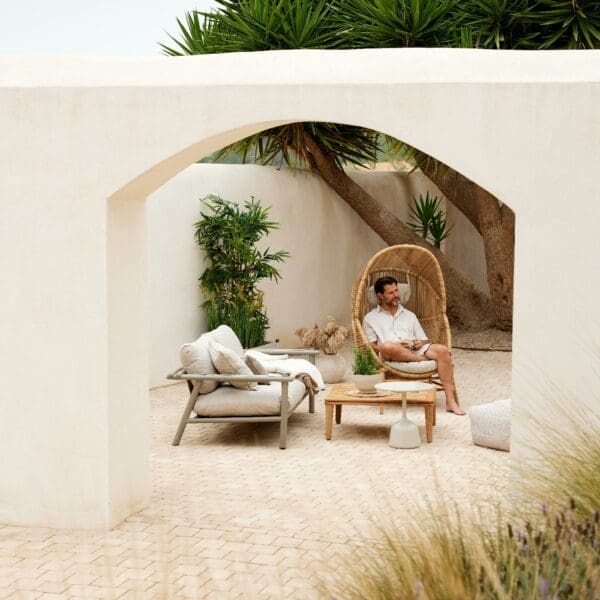 Image looking through whitewashed archway with Sticks contemporary garden sofa and man sat in Hive lounge chair