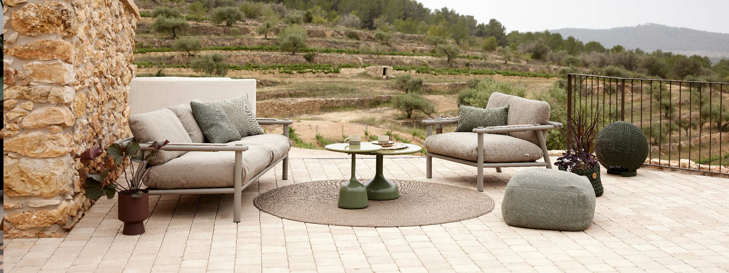 Image of Cane-line Sticks taupe coloured aluminium garden sofa and lounge chair on decking with arid terraced hillside in the background