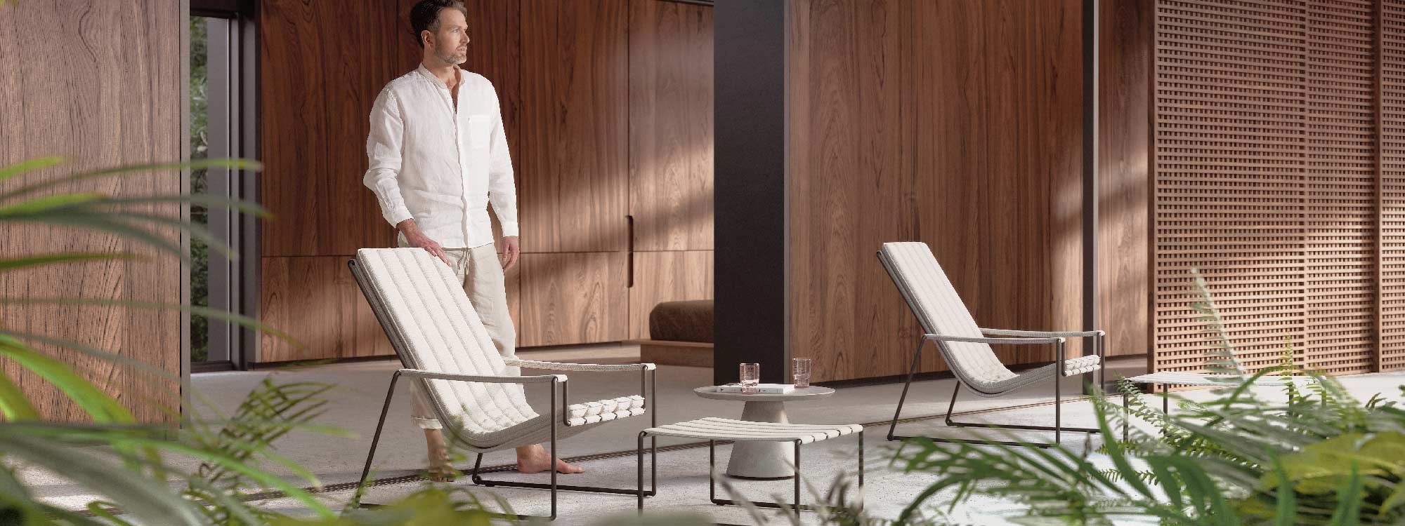 Image of man stood behind pair of Royal Botania Strappy lounge chairs with a Conix concrete side table in the middle