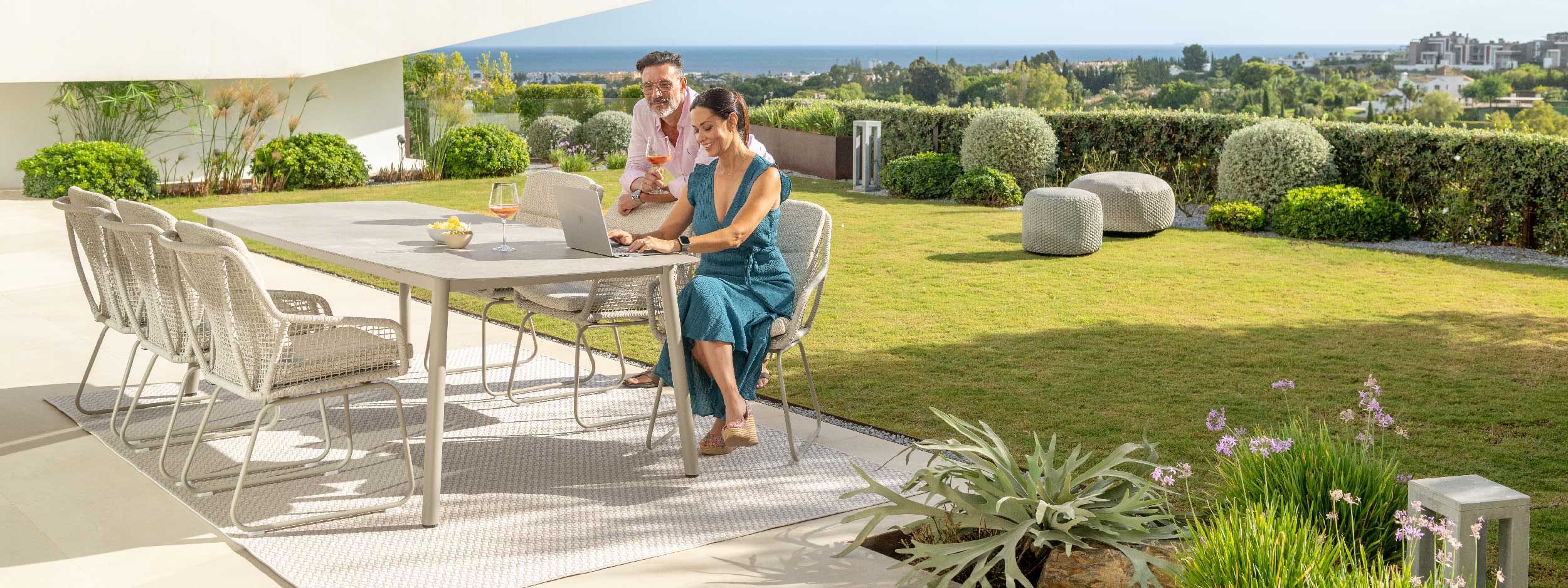 Image of couple sat on Alden contemporary garden chairs, around Durham taupe coloured table