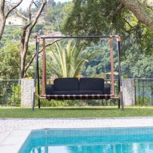 Image of Fable luxury 2 seater swing seat sofa on poolside with tree and countryside in the background