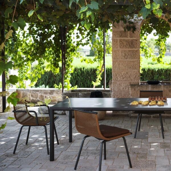 Image of Laze chairs placed around Plein Air outdoor dining table, shown beneath pergola with green vine fronds cascading down