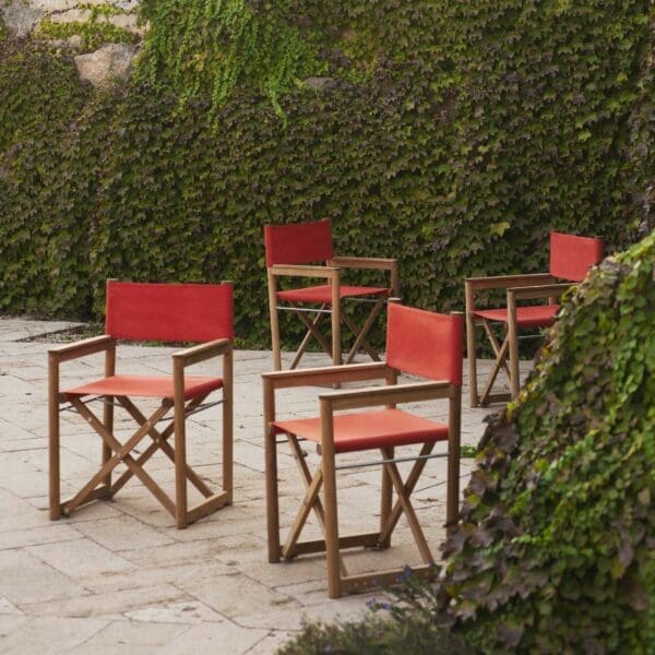 Image of several RODA Orson folding teak chairs in courtyard with creepers growing down the wall in the background