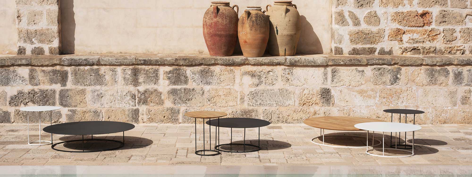 Image of different sizes and finishes of Zefiro circular low tables, in full sunshine on rustic terrace