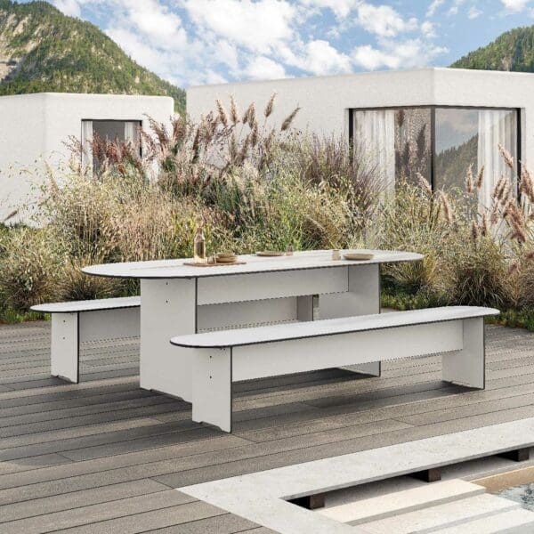 Image of RIVA ROUND minimalist garden table and benches in white HPL, shown on decking with grasses and Miscanthus grasses in the background