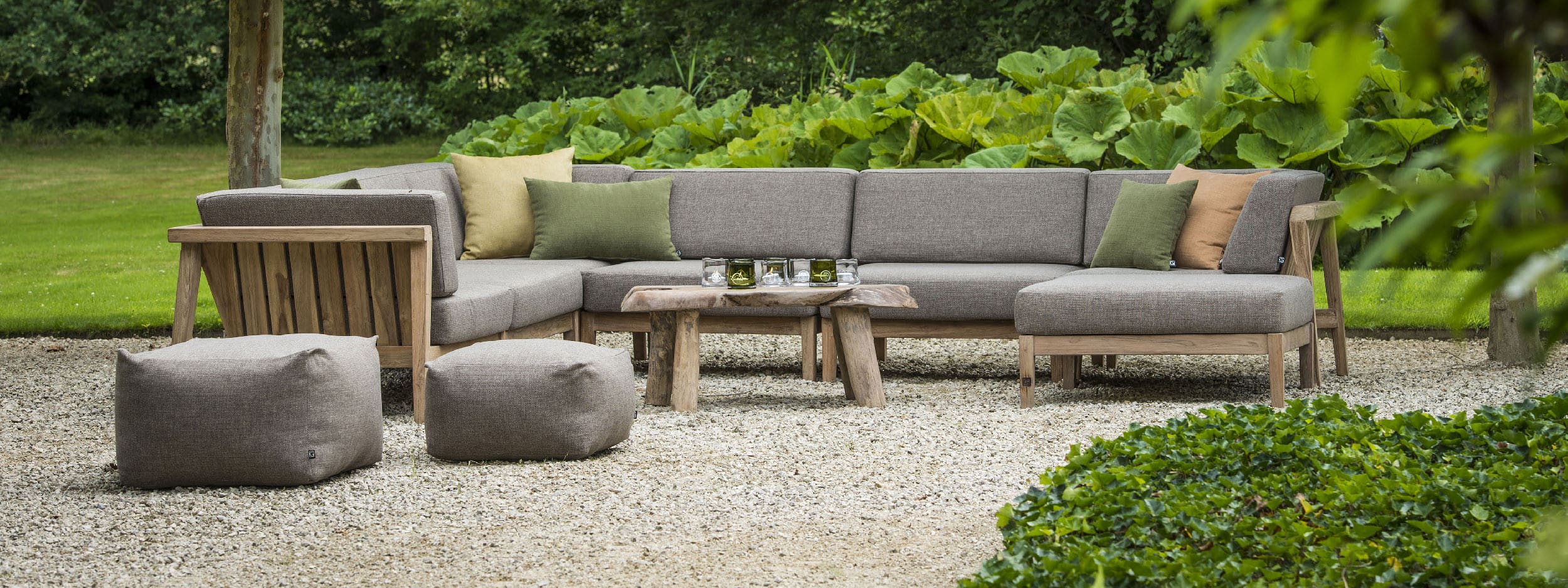 Image of Copenhague teak corner sofa with large Gunnera leaves in the background, by Gommaire luxury outdoor furniture